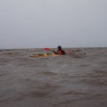 Жмёмся к берегу, из воды
повсеместно торчит тростник.

19:50. Достигли устья реки Онеги.
Надо бы его пересечь, но оно шириной почти 3 км. А отходить от берега сейчас
совсем не хочется. Вдоль берега втягиваемся в речку. На берегу начинается
какая-то промышленная зона с причалами, как потом выяснилось, «Онежский ЛДК»
(лесопильно-деревообрабатывающий комбинат). Прямо перед ним полянка.
Высаживаюсь на ней для замены батареек в навигаторе (на воде их мокрыми солёными
руками принципиально не меняю). Уже пройдено 19 км. Лёха хочет тут встать на
ночь, прямо под бетонным забором комбината. Удобное место для старта на Кий, но
нас видимо ожидают несколько дней нелётной погоды, судя по прогнозу, а торчать
несколько дней под стенами комбината вплотную к населённому пункту мне не
захотелось. Я бы встал на другом берегу Онеги. Подискутировали на этот счёт и
двинулись дальше вдоль берега вверх по реке присматривая место, что бы её
пересечь. А море нагнало в реку хорошую волну. Я стал пытаться пересечь реку,
но в сотне метров от берега так прокатился на попутной волне, что поджав хвост
быстро вернулся под берег. Лёха гребёт следом. Поднявшись по речке на 2 км
разворачиваю нос в сторону моря и по диагонали в направлении противоположного
берега начинаю пересекать русло. Так я двигаюсь против волн под острым углом.
Вполне безопасно. Лёха, не разгадав моего&nbsp;
маневра, сразу начинает пересекать по кратчайшему расстоянию, подставив
валам, катящимся с моря, свой борт. Страшно на это смотреть. &nbsp;&nbsp;

21:05. Мы уже у противоположного
берега, точнее у кромки тростниковых зарослей, которые отделяют нас от берега.ВИДЕО на YuoTubeЗамерили ветер прямо из лодки.
Средняя скорость 6.9 м/с, порывы до 8.4 м/с. Надо вставать. И ветер уже
некомфортный, и почти сутки не спали. Но к берегу не подойти из-за тростника. На
берегу виднеется избушка, до неё по тростнику метров 500. Но я бы предпочёл
километров 10 грести, чем 500 метров тащить. &nbsp;Начинаем вдоль тростника плыть в сторону моря.
Как вышли из устья, то стало очень мелко. К тому же начался отлив. Обогнули мыс
Пильский. Я незаметно от себя убежал от Лёхи. Пришлось вернуться. Лёха тем
временем вылез из лодки и ведёт её как кораблик.&nbsp;